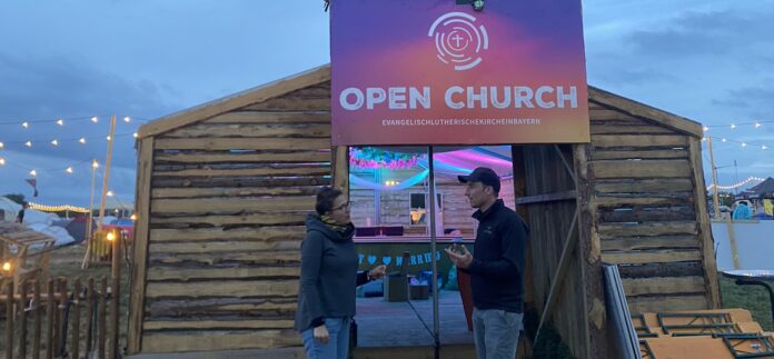 Mitten im Festival: Pfarrerin Meike Müller-Stach spricht vor der „Open Church“ mit einem Festivalbesucher. Die kleine Holzkirche ist Anlaufstelle für Seelsorge, Begegnung und kurze Auszeiten. Foto: Privat